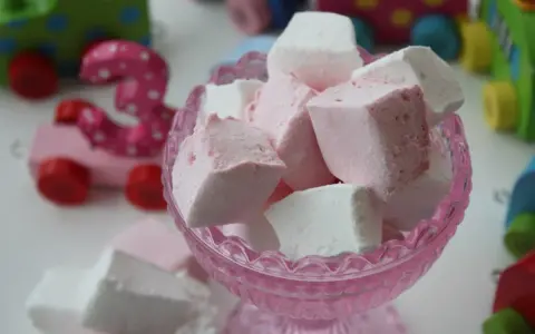 En skål med hemmagjorda marshmallows i rosa och vitt. I bakgrunden syns färgglada träleksaker, som en rosa bil med siffran 3.