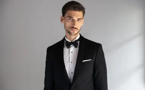 Elegancki mężczyzna w czarnym smokingu z białą poszetką. Dowiedz się, jak dobrać poszetkę do stylizacji.