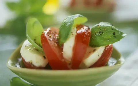 Tomate Mozzarella, ein gesundes Gericht, garniert mit frischem Basilikum und Pfeffer, serviert in einer grünen Schale.