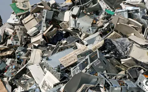 Góra starych komputerów, monitorów i klawiatur. To widok na odpady przemysłowe, które czekają na recykling.