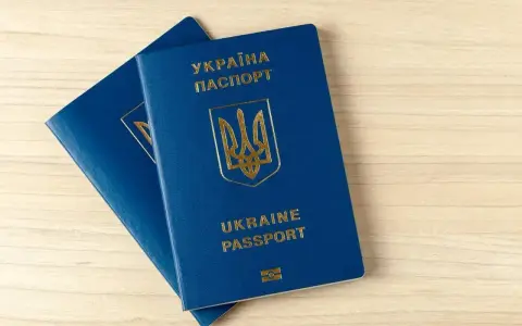 Dwa niebieskie paszporty biometryczne Ukrainy z złotym godłem i napisami leżą na drewnianym blacie.