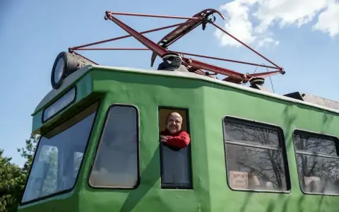 Uśmiechnięty mężczyzna w czerwonym swetrze wygląda z okna zielonej lokomotywy. To łódź Skierniewice, gotowa do podróży.