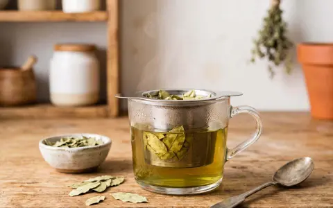 Infusion de feuille de séné, danger potentiel pour la santé. Une tasse de thé fumant avec des feuilles dans un infuseur, à côté d'un bol de feuilles séchées et d'une cuillère.