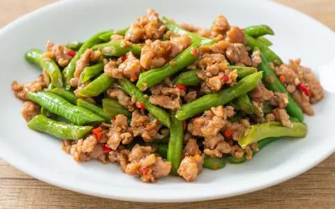 Fasolka szparagowa z mielonym mięsem i papryczką chili na białym talerzu.
