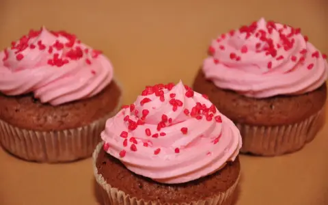 Tre chokladmuffins med rosa frosting och röda strössel, bakade i rosa muffinsformar.