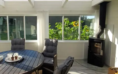 Mysig kamin i uterummet med solrosor utanför fönstret. Ett runt bord med stolar står redo för fika.