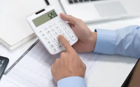 Persona calculando en calculadora blanca, revisando documentos y tablet. Se pregunta cuánto cuesta abrir una empresa en España.