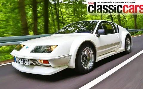Weißer Renault Alpine A310 fährt auf einer Straße durch einen grünen Wald.