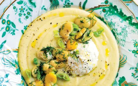 Macco di fave fresche cremoso, guarnito con fave intere, ricotta fresca e aneto, servito su un piatto decorato.