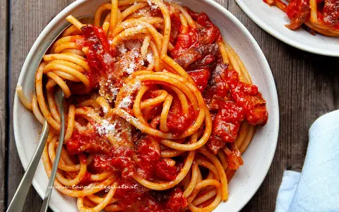 Un piatto fumante di spaghetti conditi con un ricco sugo all'amatriciana ricetta della nonna, cosparso di formaggio grattugiato.