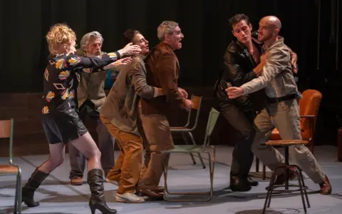 Scène de théâtre tendue. Des hommes se disputent, leurs gestes évoquent une lutte. La scène rappelle la conjugaison du verbe "aboyer" dans un moment de tension.