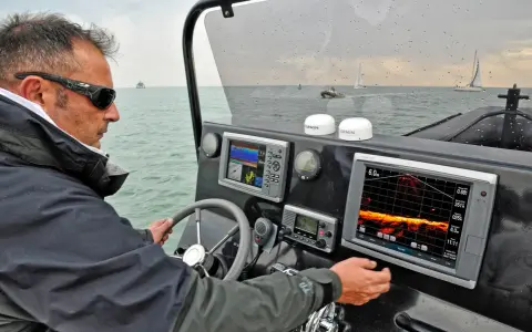 Un homme navigue, consultant un écran de sonar affichant des données sous-marines.