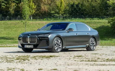 Elegancki, grafitowy BMW 740d na tle zieleni. Luksusowa limuzyna prezentuje się imponująco.