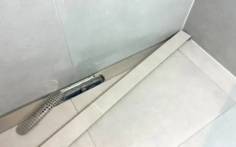 En dusch med en Purus vakuumventil och ett perforerat galler. Vatten droppar på de ljusa kakelplattorna.