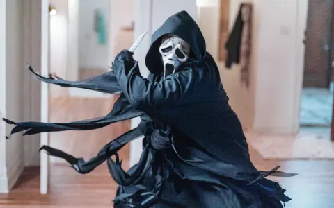Ghostface, icona del film horror slasher, brandisce un coltello in un corridoio.
