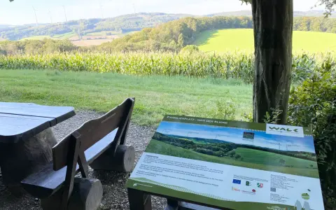 Holzbänke und ein Tisch laden zum Verweilen ein. Ein Schild "Familienplatz - Weg der Blicke" weist auf die Aussicht hin.