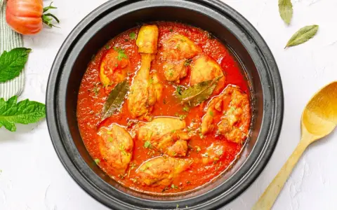 Pollo en salsa de tomate casera en olla negra, con hojas de laurel y perejil picado.