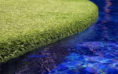 A vibrant green artificial grass island floats in a bright blue pool. The question of will chlorine kill grass is answered by this synthetic turf, unaffected by the water.