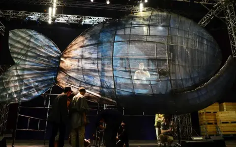 Scena teatralna z wielką, szklaną rybą, w której siedzi człowiek. To może być cud Jonasza.