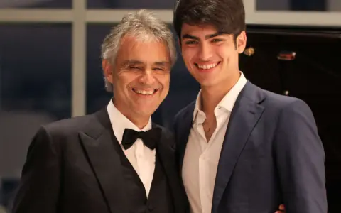 Andrea Bocelli młody i jego syn Matteo, obaj uśmiechnięci, w eleganckich strojach.
