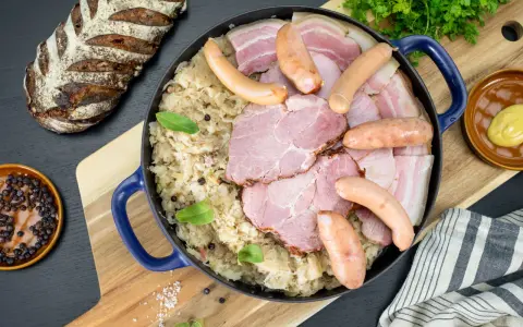 Un plat généreux de choucroute de Noël, garni de saucisses, jambon et lard, accompagné d'une miche de pain rustique.