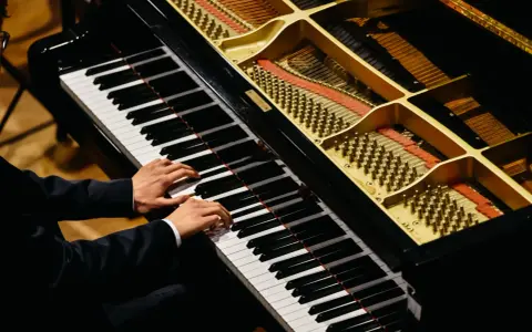 Dłonie muzyka grające na fortepianie, którego wnętrze z widocznymi strunami i młoteczkami przypomina zaawansowany piano vst.