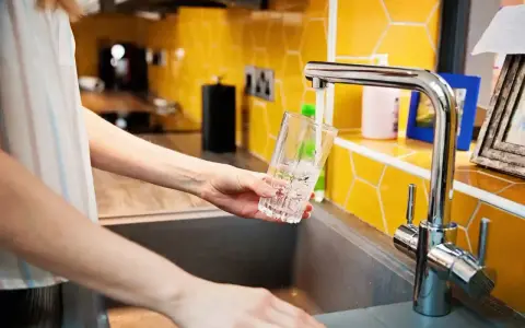 Ręka nalewa wodę do szklanki z kranu. To jak małe złoże do stacji uzdatniania wody w domu, zapewniające czystość.