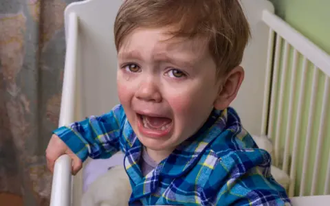 Niño de 10 años llorando en su cuna, se comporta como bebé.