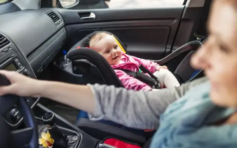 Uśmiechnięte dziecko w foteliku z przodu. Od kiedy dziecko może jeździć z przodu, zależy od jego wieku i wagi.
