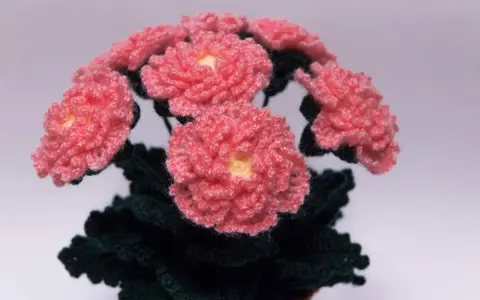 En bukett av virka blommor i rosa med gula mittar och mörkgröna blad.