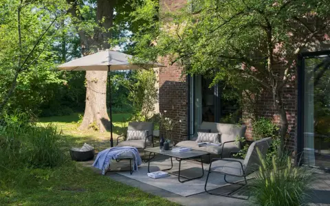 Gemütliche kleine Terrasse gestalten mit bequemen Sitzmöbeln, Tisch, Sonnenschirm und Kissen. Einladend und grün.