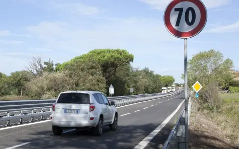 Un'auto bianca percorre una strada extraurbana secondaria, superando un cartello di limite di velocità a 70 km/h.