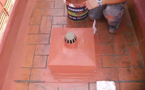 Persona aplica pintura para impermeabilizar terraza. Cubeta de Mariseal y desagüe en el centro.