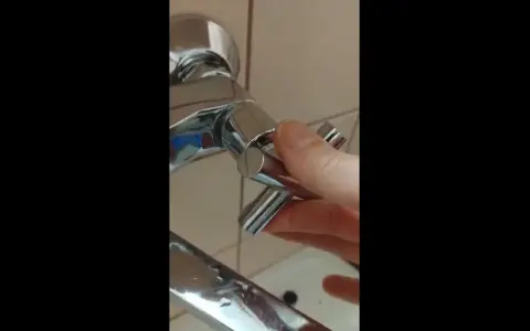 Dłoń odkręca chromowany kurek z baterii prysznicowej. Prosty poradnik, jak zdjąć kurek z kranu.