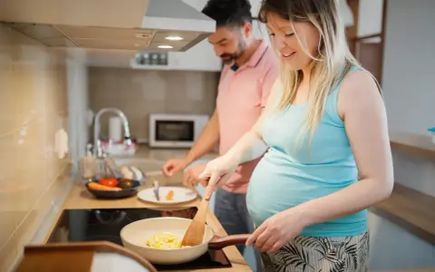 Schwangere Frau kocht Rührei, während ihr Mann daneben steht. Sie achtet auf ihre Ernährung, um Listeriose in der Schwangerschaft zu vermeiden.
