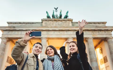 Tre glada vänner tar en selfie framför Brandenburger Tor, en ikonisk sevärdhet att se i Berlin.