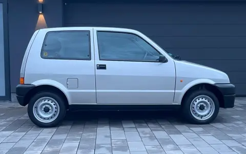 Srebrny Fiat Cinquecento na tle ciemnego garażu, z charakterystycznymi felgami i czarnymi zderzakami.