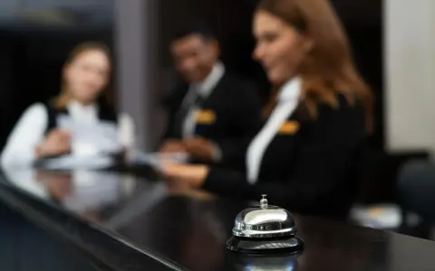 Dzwonek przy ladzie hotelowej, gdzie pracownicy obsługują gości. Stanowiska pracy w hotelu tętnią życiem.