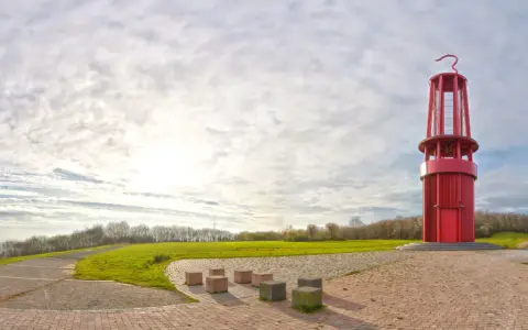 Rote Aussichtsturm auf der Halde Moers, umgeben von grünen Hügeln und einem weiten Himmel mit Wolken.