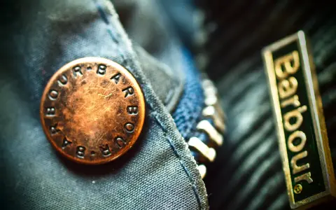 Detale kurtki Barbour: mosiężny guzik z logo i naszywka z nazwą firmy. Barbour to znana marka odzieży.