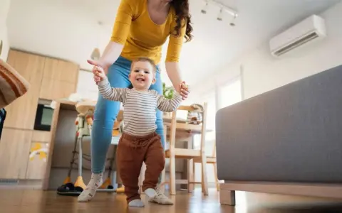 Mamá ayuda a su bebé a dar sus primeros pasos en una habitación cómoda, con el aire acondicionado bebes funcionando para mantener la temperatura ideal.