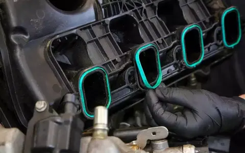 A gloved hand installs a new intake manifold gasket, ensuring a tight seal for optimal engine performance.
