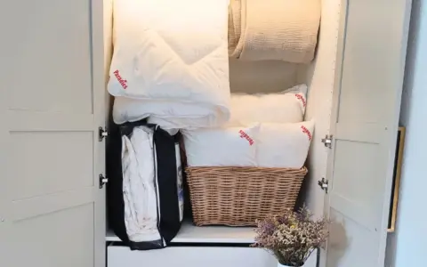 Ordentlich verstaut: weiße Bettdecke falten und Kissen im Schrank, daneben eine Decke und ein Korb mit Bettzeug.