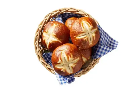 Koszyk z kilkoma bułkami bawarskimi, ułożonymi na niebiesko-białej kratkowanej serwetce.