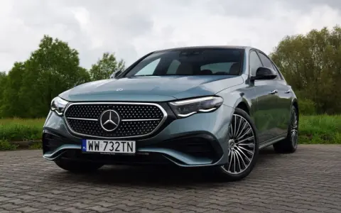 Elegancki Mercedes E220d w kolorze miętowym, zaparkowany na brukowanej nawierzchni, z zielenią w tle.