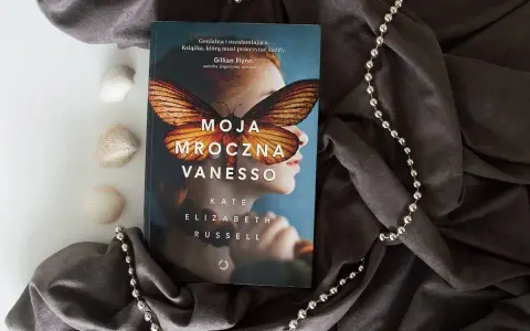 Okładka książki "Moja mroczna Vanesso" z motywem motyla na twarzy dziewczyny, otoczona szarym materiałem i koralikami.