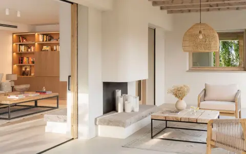 Salón luminoso con chimenea de piedra, muebles de madera y textiles naturales, evocando un relajante estilo ibicenco.