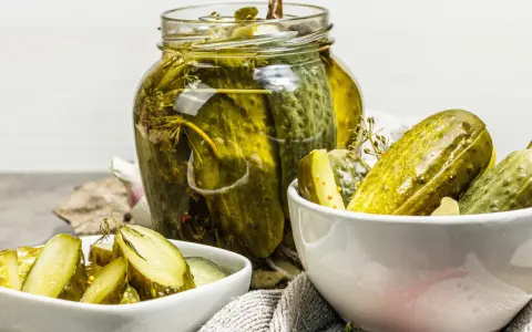 Cetrioli in agrodolce in un barattolo di vetro e in ciotole, con aglio e spezie.