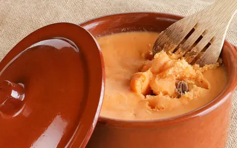 Un cuenco de barro con lomo en manteca, listo para ser servido. Una cuchara de madera remueve la deliciosa preparación.