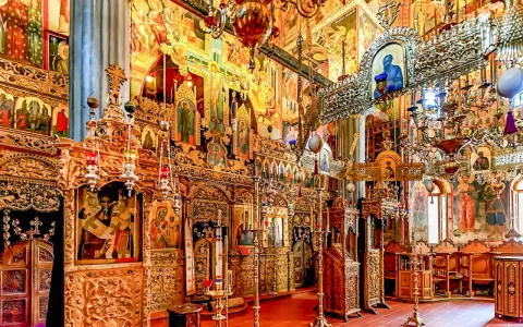 Interior of a richly decorated Orthodox church, showcasing ornate iconostasis, frescoes, and chandeliers, typical of many ancient christian monasteries.